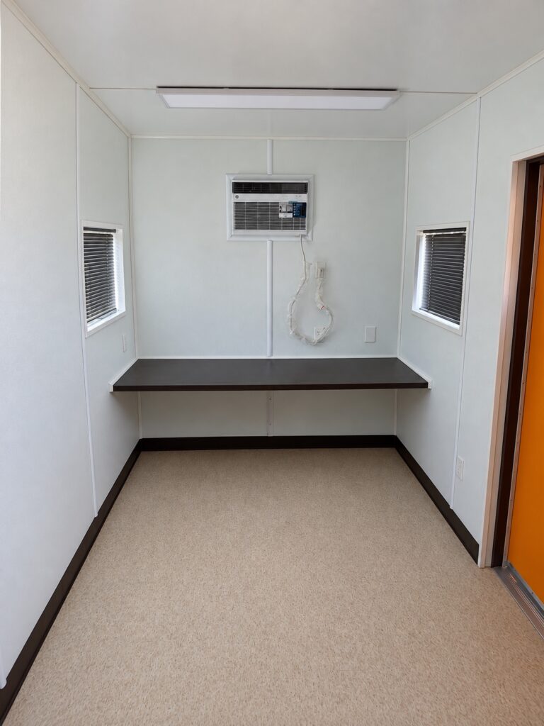 Inside a 20 foot container office with countertop desk, wall air conditioner, and LED light
