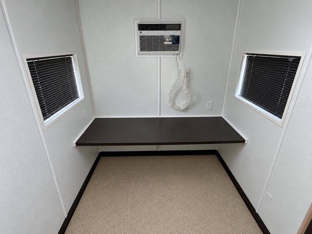 Inside a 20 foot container office with countertop desk, air conditioner, and two windows