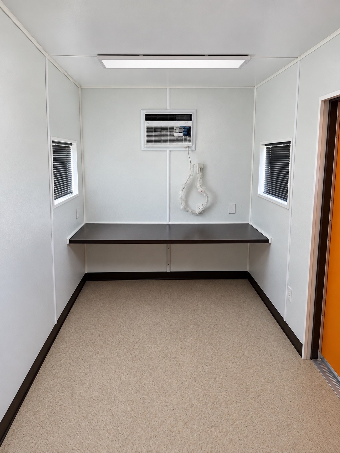 Finished container office interior with countertop desk, wall air conditioner, LED light, and access door